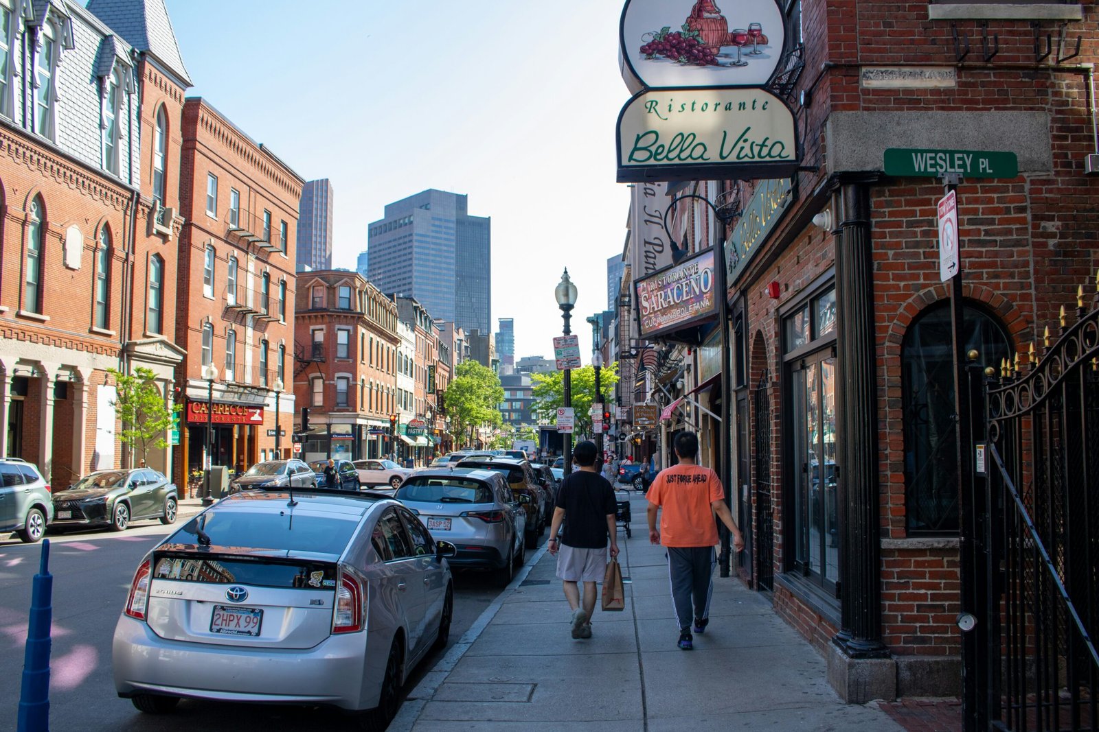 A couple of people walking down a sidewalk next to parked cars